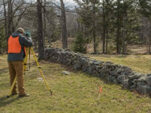 Survey total station and offset marker beside a historic New England stone wall during a boundary investigation.